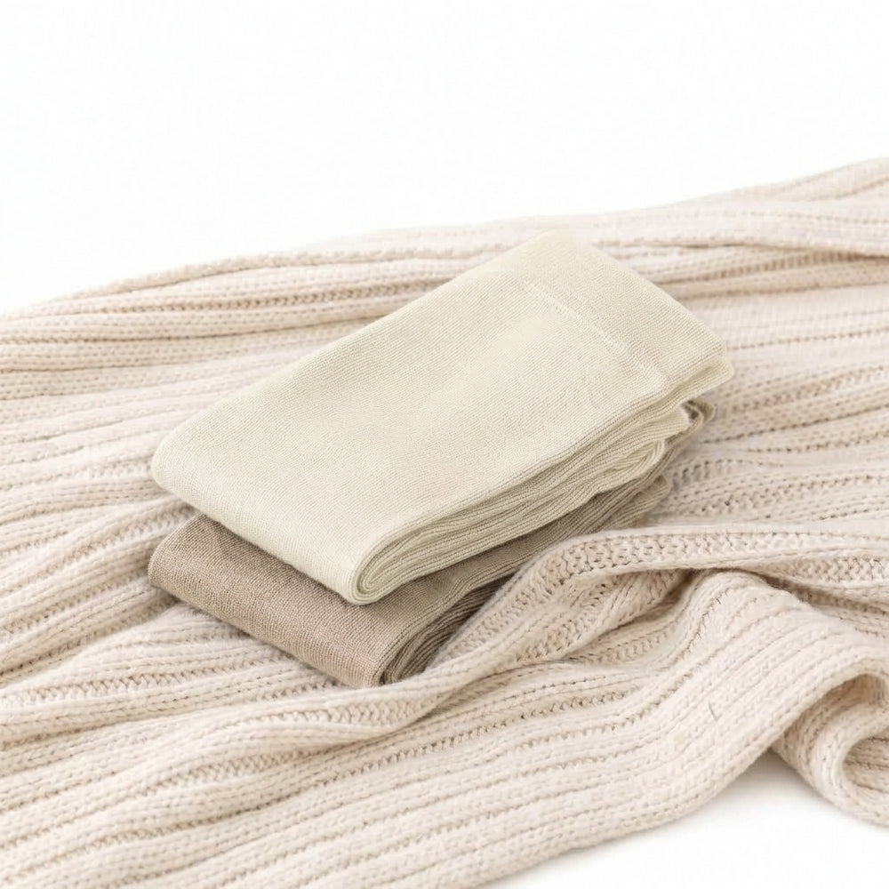 Two folded pairs of ROMATOKI merino five-toe socks in Ivory and Sand resting on a cream knit blanket
