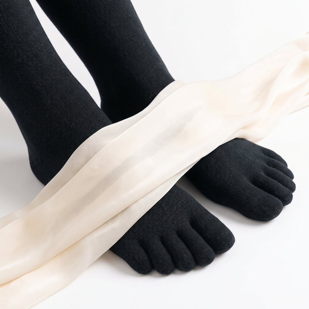 ROMATOKI merino five-toe socks in Coal worn on both feet, with a length of fine cream yarn draped across them to show how thin the knit is