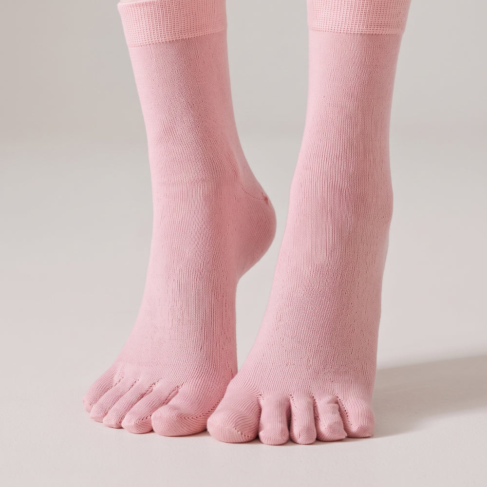 A pair of ROMATOKI merino five-toe socks in Blush worn standing on a pale floor